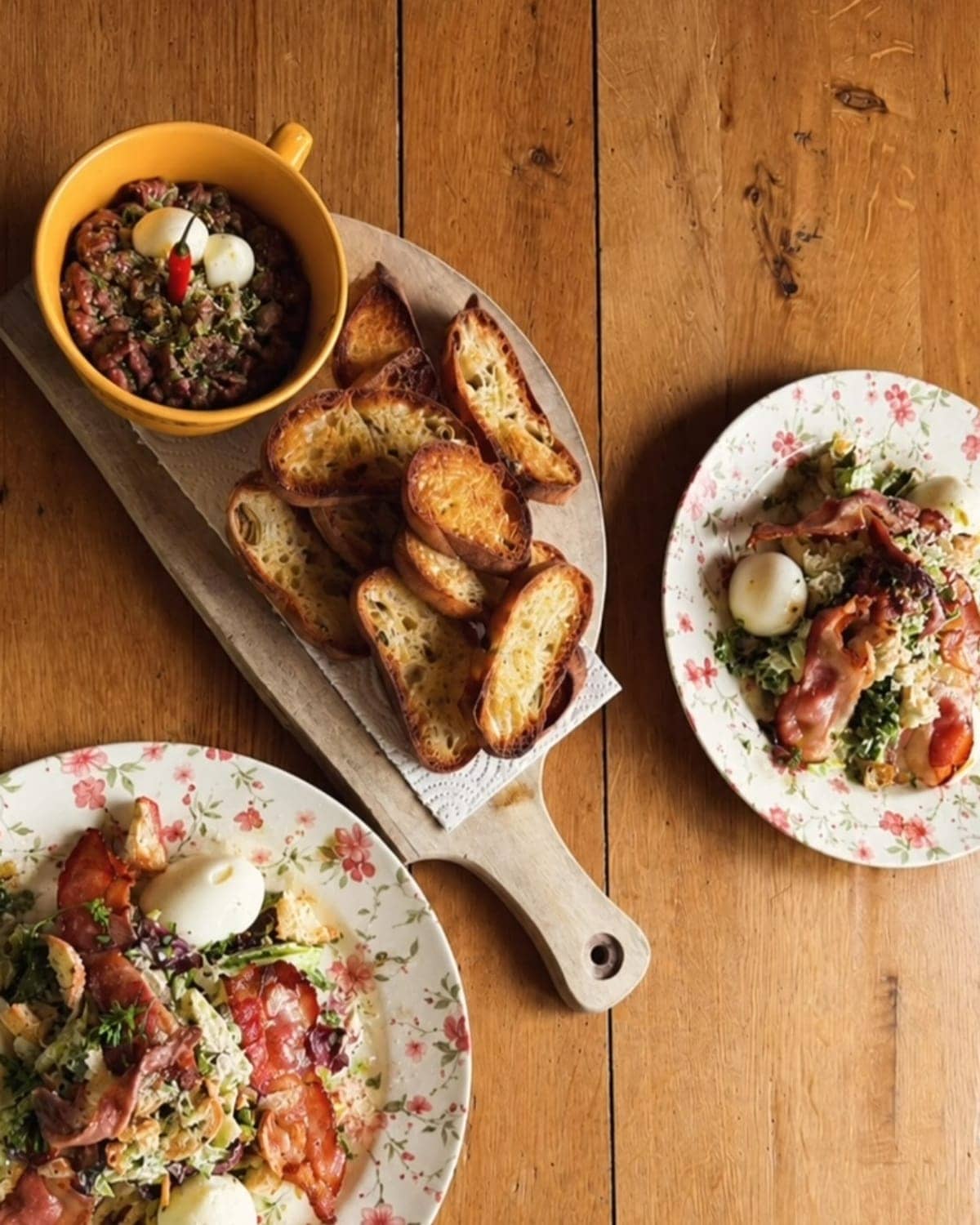 A shared table: beef tartare with toasted bread and two salads with crispy bacon and soft eggs